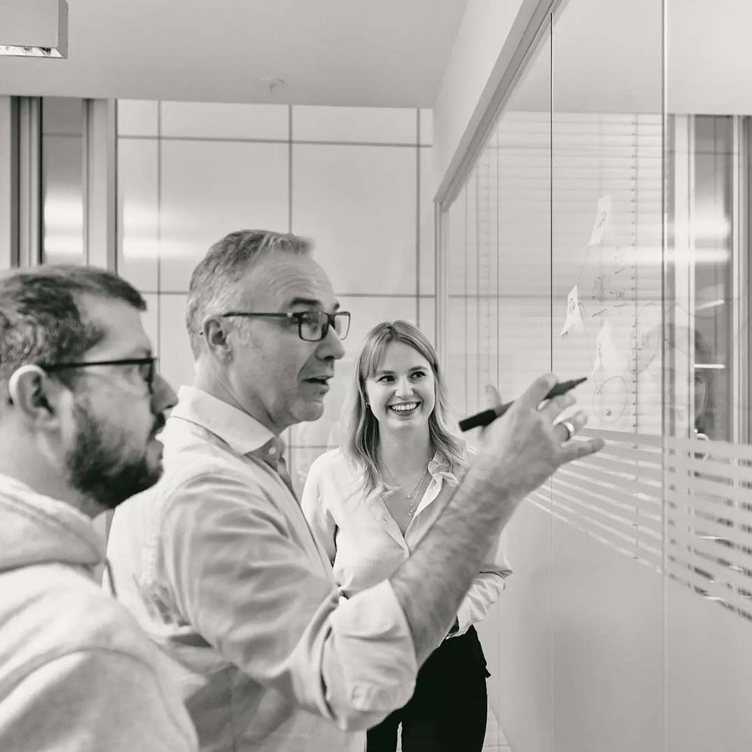 Three people from the Billwerk team talk through a plan at a glass wall.