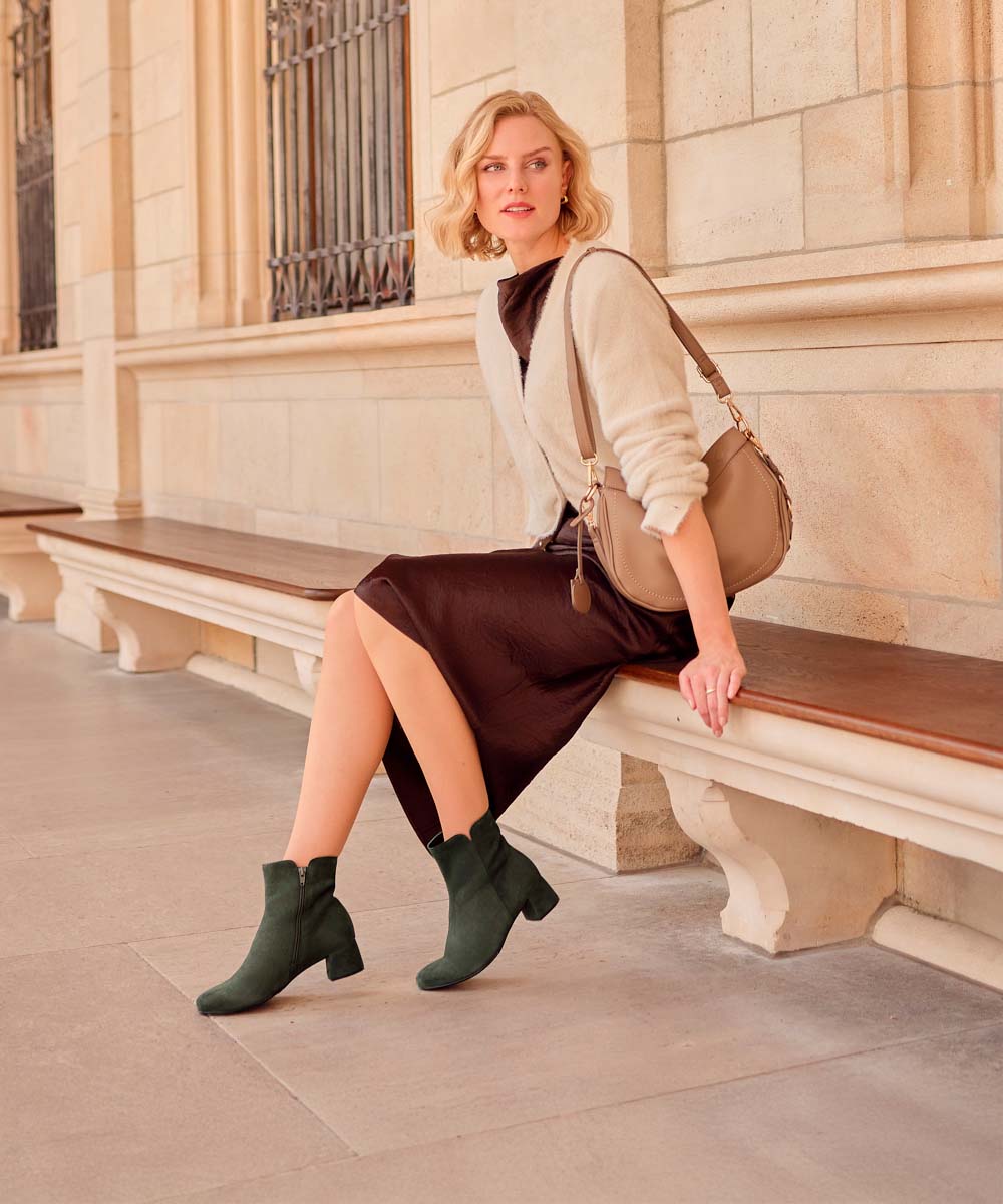 A woman in green Gabor ankle boots sits on a stone bench.