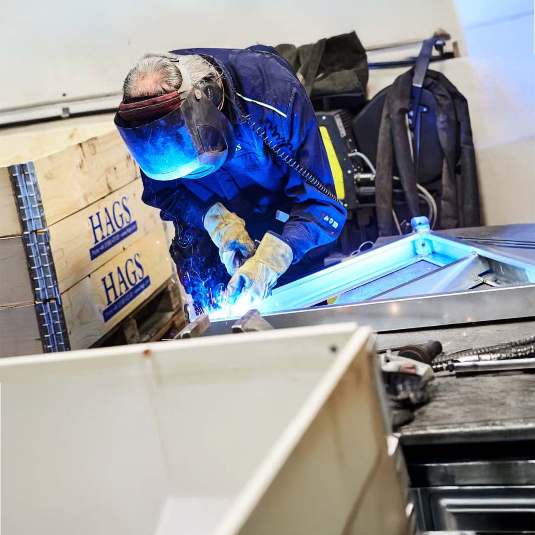 A welder at work in the HAGS factory, with HAGS crates beside him.
