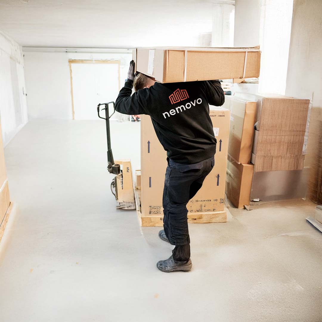 A Nemovo mover carries a large box through an empty room.