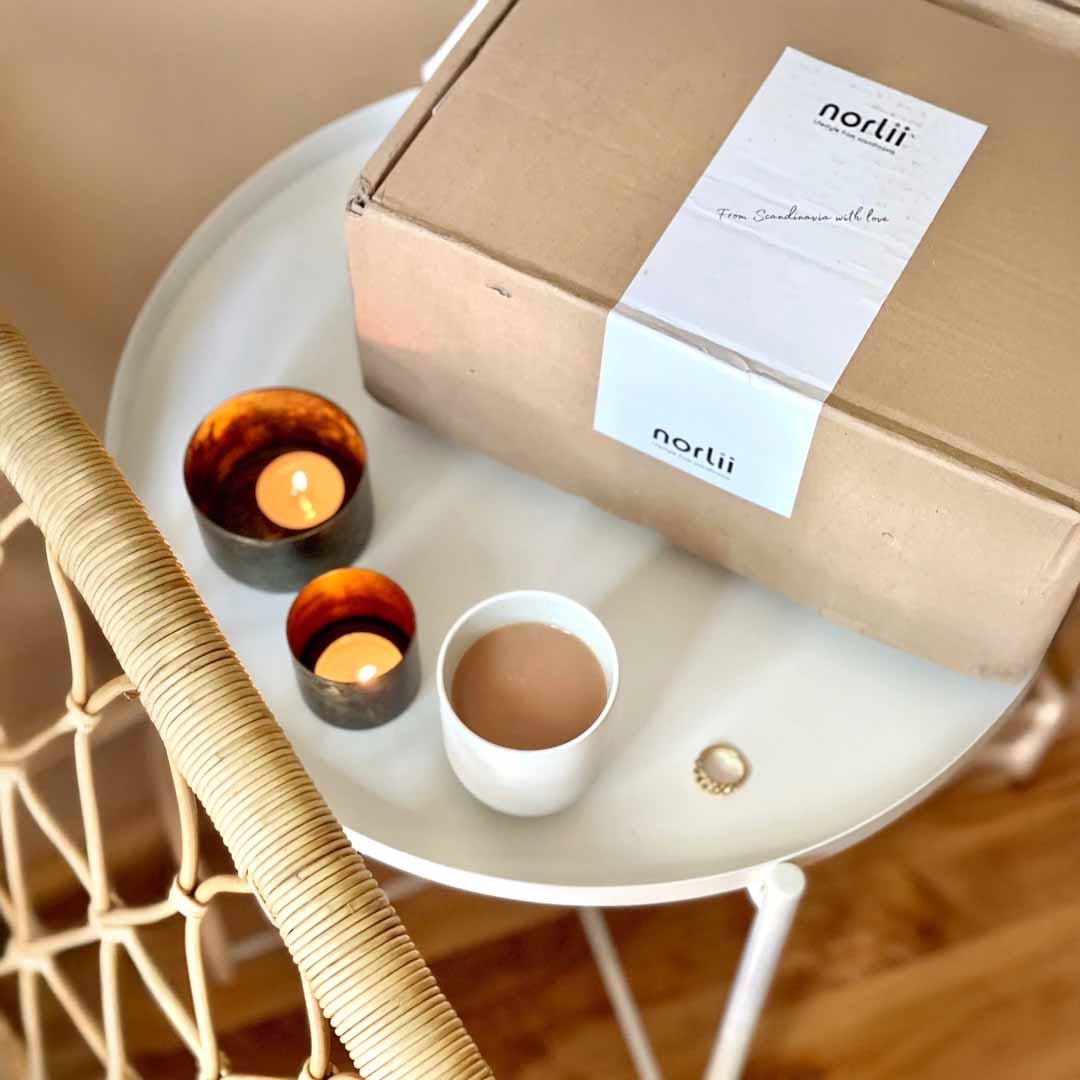 A Norlii parcel on a small table beside two candles and a cup of coffee.